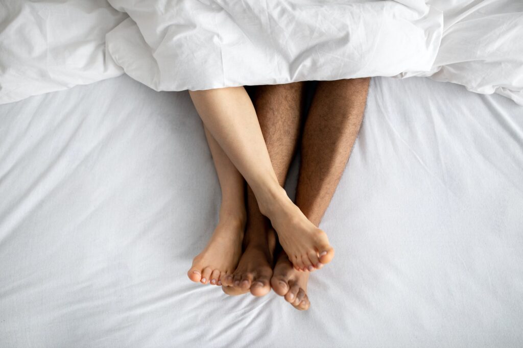 Top view of young multiracial couple lying in bed after lovemaking. Erotic games, sexual foreplay
